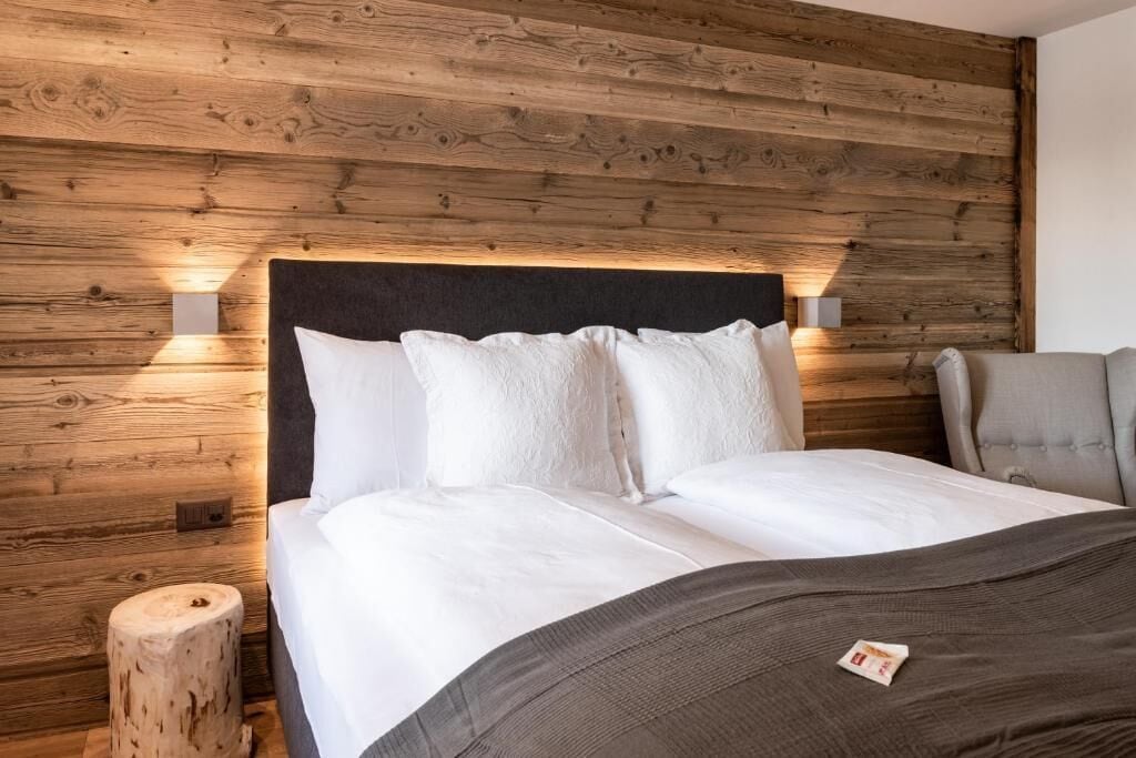 Une chambre avec un mur recouvert de panneaux de bois, un lit avec une literie blanche, une table de chevet et une chaise.