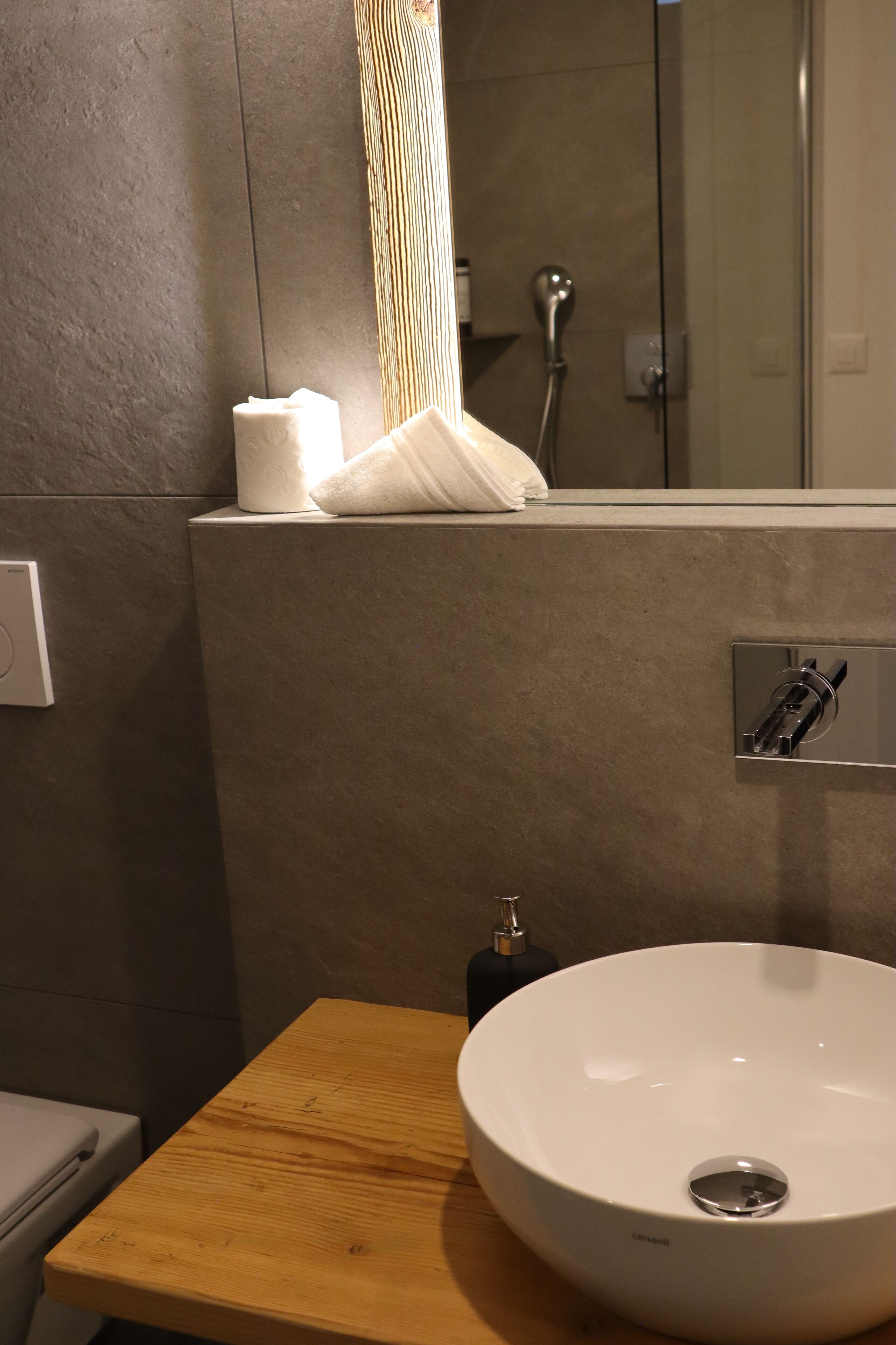 Ein Badezimmer mit einem Holzanrichte, einem weißen Waschbecken, einem Handtuchspender und einer Duschkabine.