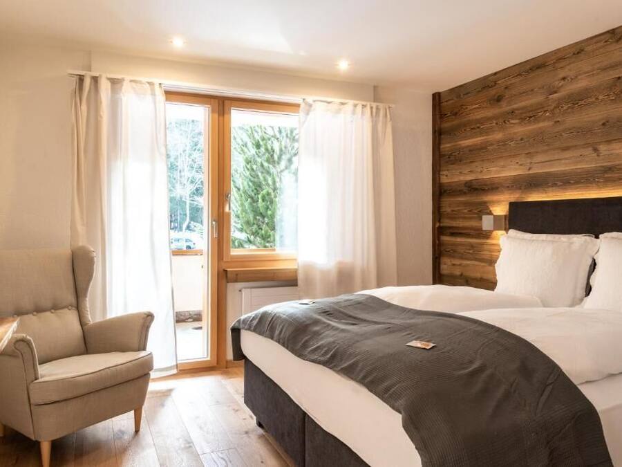 Une chambre avec un grand lit, une tête de lit en bois, une chaise et une vue à travers une porte vitrée.