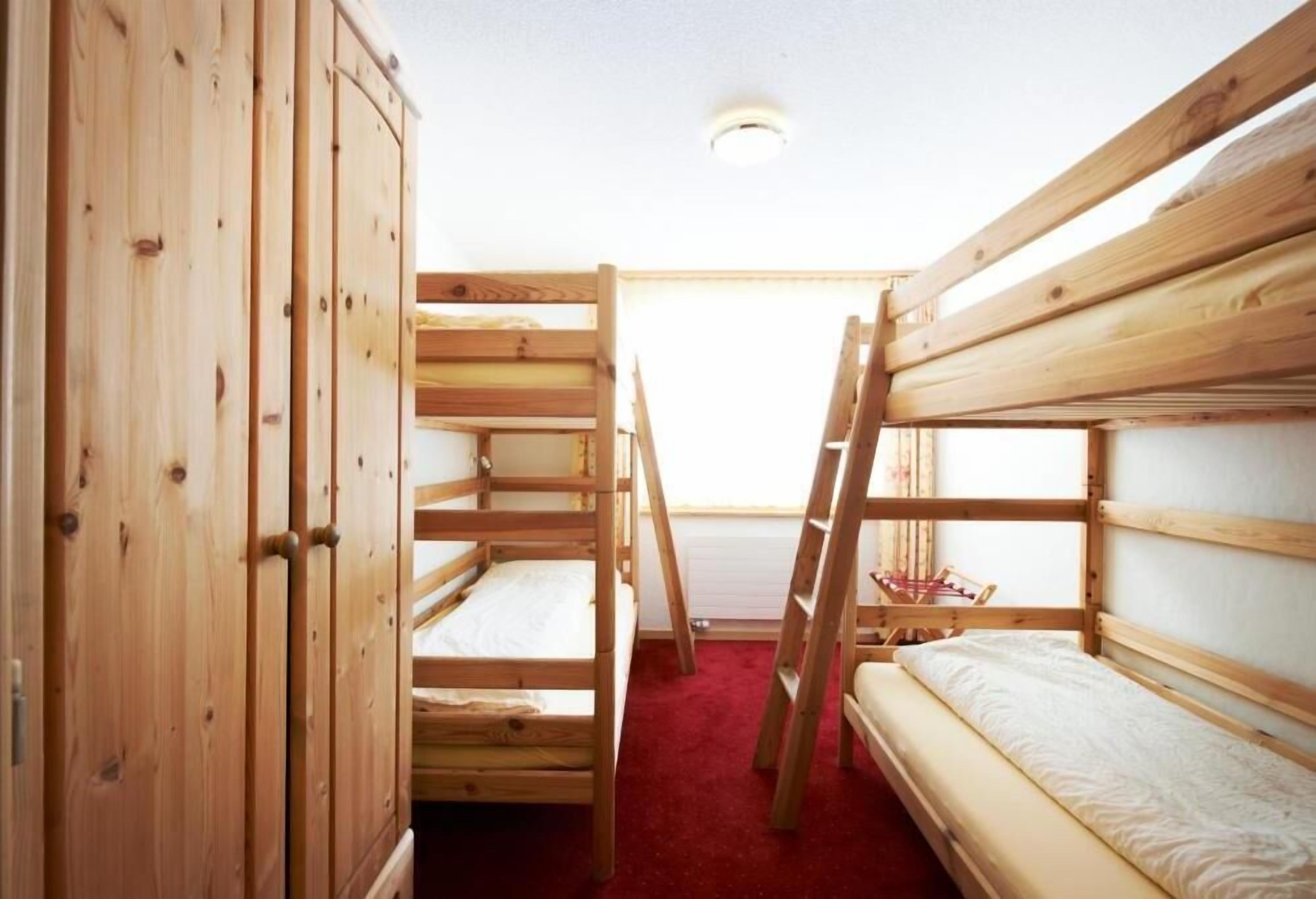 Une chambre avec des lits superposés en bois, une armoire et une échelle.