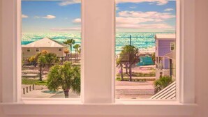 A view through a window of a coastal area with buildings, palm trees, and the ocean. - Beach Haven, Game Room, Arcades (Mexico Beach)