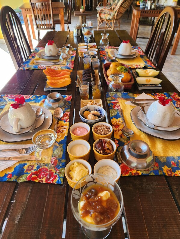 Een lange eettafel met een verscheidenheid aan gerechten en drankjes, waaronder schalen met eten, glazen met drank en een kan.
