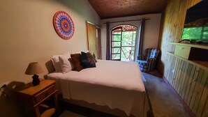 Un dormitorio con cama, mesita de noche, lámpara, silla y televisión.