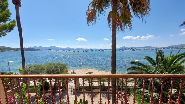 A balcony with a view of a calm sea, palm trees, and a distant mountain range. - Three bedroom apartment on the Pine Walk with superb views. WIFI and Air Con (Pollença)