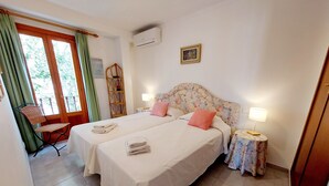 A hotel room with two beds, a chair, a small table, and a window with curtains. - Three bedroom apartment on the Pine Walk with superb views. WIFI and Air Con (Pollença)