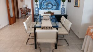 A dining area with a glass table, white upholstered chairs, and a blue abstract painting on the wall. - Three bedroom apartment on the Pine Walk with superb views. WIFI and Air Con (Pollença)