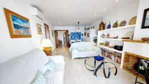 A modern living room with a white sofa, a coffee table, and a bookshelf filled with books. - Three bedroom apartment on the Pine Walk with superb views. WIFI and Air Con (Pollença)