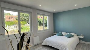 Une chambre avec un grand lit, deux fenêtres, un tapis rond et un vase contenant des plantes séchées.