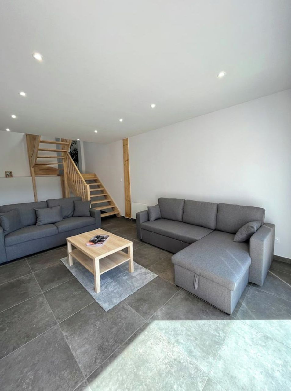 Un salon moderne avec deux canapés gris, une table basse en bois et un escalier en bois.