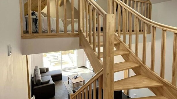 Un escalier en bois menant à une chambre aménagée en mezzanine, un salon moderne avec un canapé et une table basse, et des fenêtres de toit.