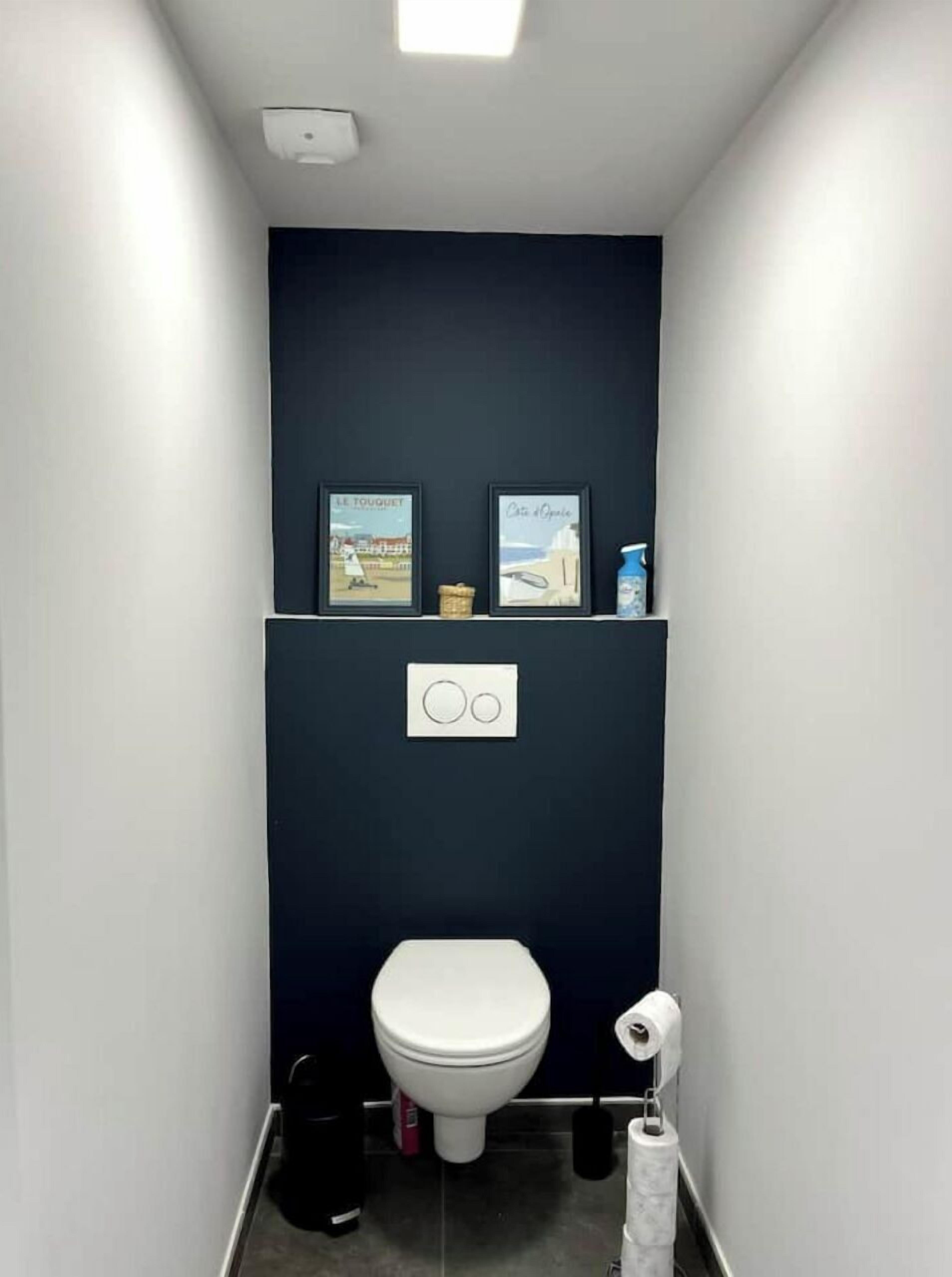 A narrow bathroom with a white toilet, a small trash bin, and a toilet paper holder.