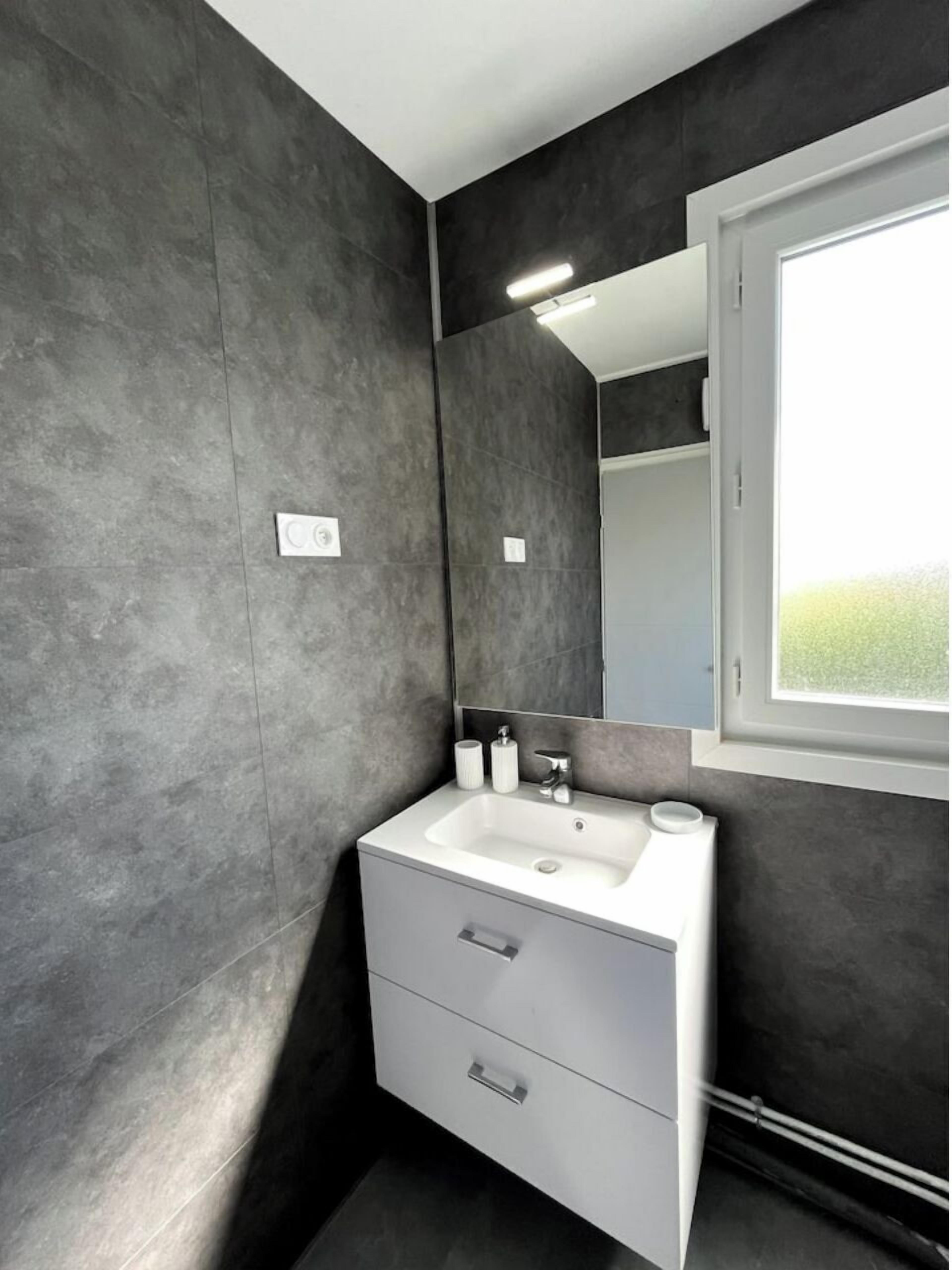 Un baño moderno con un lavamanos blanco, un espejo y una ventana.