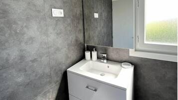 Un baño moderno con un lavamanos blanco, un espejo y una ventana.