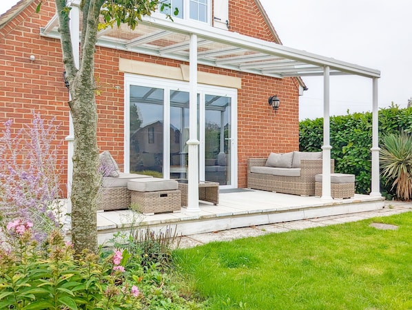 A house with a covered patio, a brick exterior, and a glass door leading to a garden.