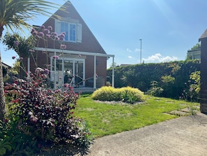 A house with a brick exterior, a glass door, and a garden with various plants and a lawn.