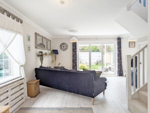A spacious living room with a dark blue sofa, a wooden cabinet, and a large window with sheer curtains.