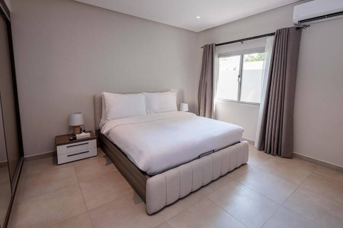 Un dormitorio con cama, mesitas de noche, una ventana con cortinas y un equipo de aire acondicionado.