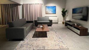 A modern living room with a sectional sofa, a coffee table, a TV, and a large window with curtains. - Nordic Gardens (Jannusan)