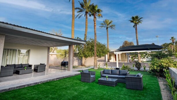 A modern outdoor patio with a sofa set, a barbecue grill, and palm trees. - Nordic Gardens (Jannusan)