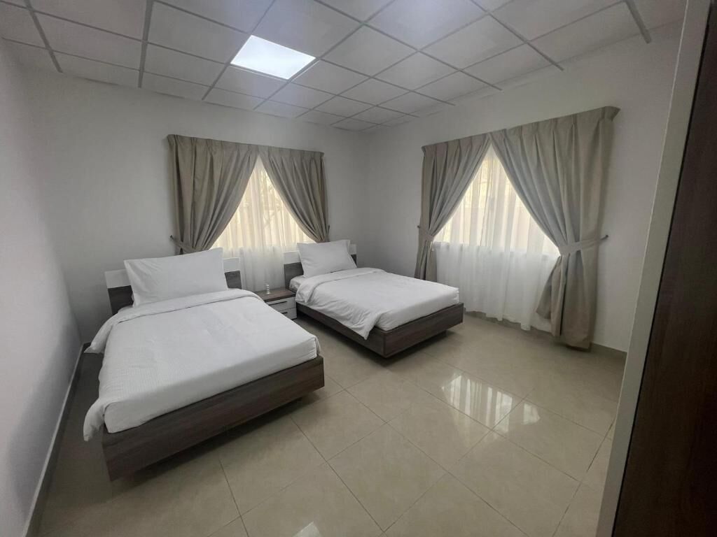 Une chambre avec deux lits, un luminaire au plafond et des rideaux aux fenêtres.