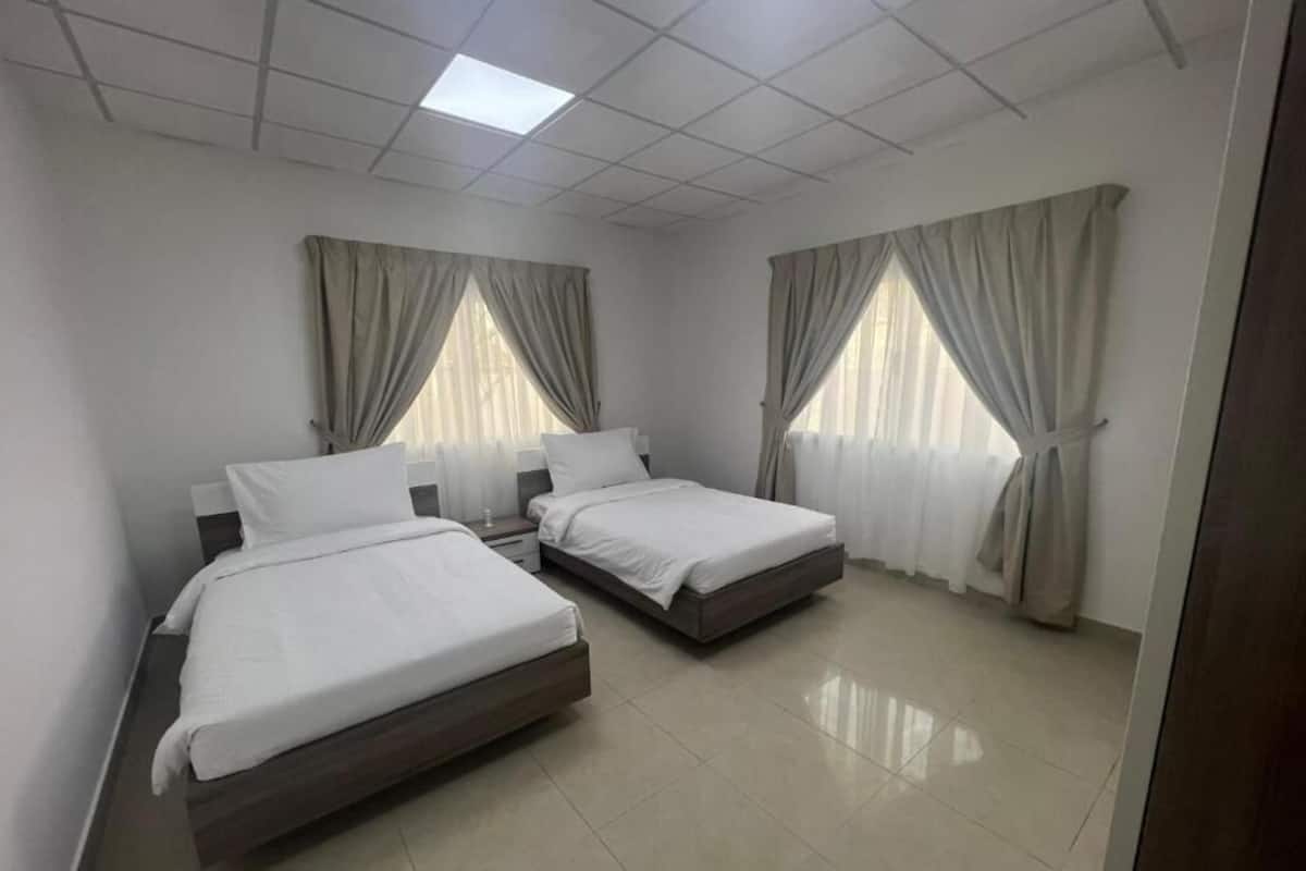 Una habitación con dos camas, una lámpara en el techo y cortinas en las ventanas.