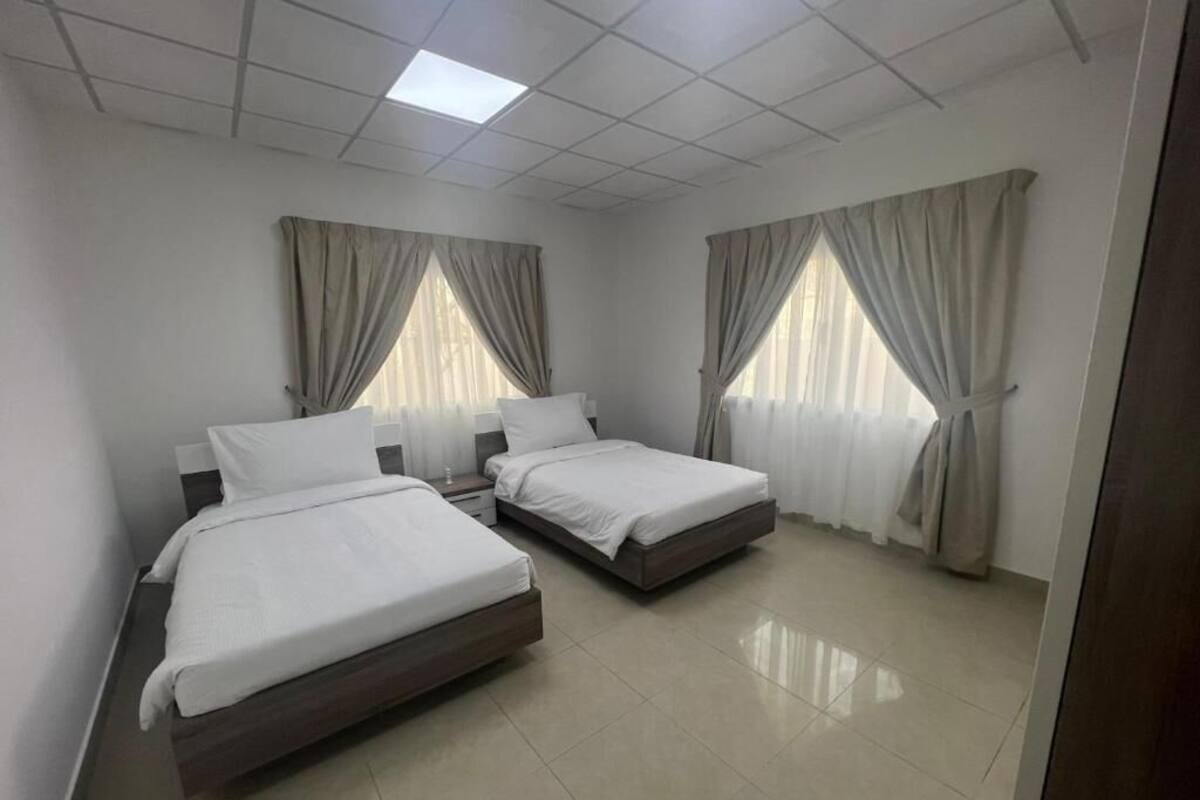 Une chambre avec deux lits, un luminaire au plafond et des rideaux aux fenêtres.