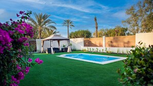 A backyard with artificial grass, a swimming pool, a gazebo, and a wooden fence. - Nordic Gardens (Jannusan)