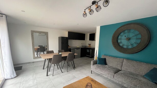A modern living room with a sofa, coffee table, and dining area. - Appartement T3 au RDC dans résidence sécurisé avec terrasse et barbecue (Martigues)