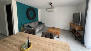 A modern living room with a sofa, a coffee table, and a television. - Appartement T3 au RDC dans résidence sécurisé avec terrasse et barbecue (Martigues)