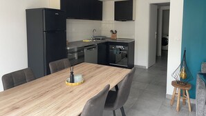 A modern kitchen with black cabinets, a wooden dining table, and a built-in oven. - Appartement T3 au RDC dans résidence sécurisé avec terrasse et barbecue (Martigues)
