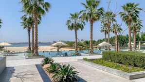 A resort pool area with palm trees, a beach view, and a clear sky. - Picturesque 3BR with Assistant Room at The One JBR by Deluxe Holiday Homes (Dubai)