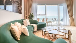 A modern living room with a green sofa, a glass coffee table, and a view of the sea through large windows. - Picturesque 3BR with Assistant Room at The One JBR by Deluxe Holiday Homes (Dubai)