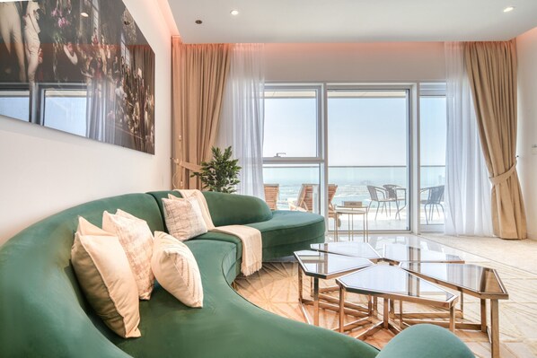 A modern living room with a green sofa, a glass coffee table, and a view of the sea through large windows.