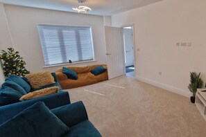 A living room with a sofa, a coffee table, and a potted plant. - Peterborough - House - Sleeps 8 - Parking - Garden (Peterborough)