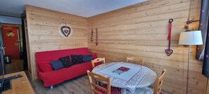 Una habitación acogedora con sofá rojo, paredes de madera, una mesa redonda con mantel blanco y adornos con forma de corazón.