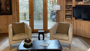 A cozy living room with two armchairs, a coffee table, and a television. - Walk to Waterfalls!  Cozy All Seasons Highlands Cabin 6 min to Town (Highlands)