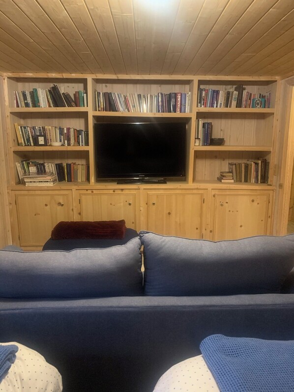 Un salon avec un canapé, un téléviseur et des étagères en bois remplies de livres.