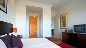 Quarto de hotel com uma cama grande, televisão, escrivaninha e banheiro visível através de uma porta aberta.