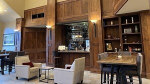 Une pièce spacieuse avec des lambris en bois, un coin bar avec des étagères remplies de bouteilles, et un espace repas avec des chaises et une table.