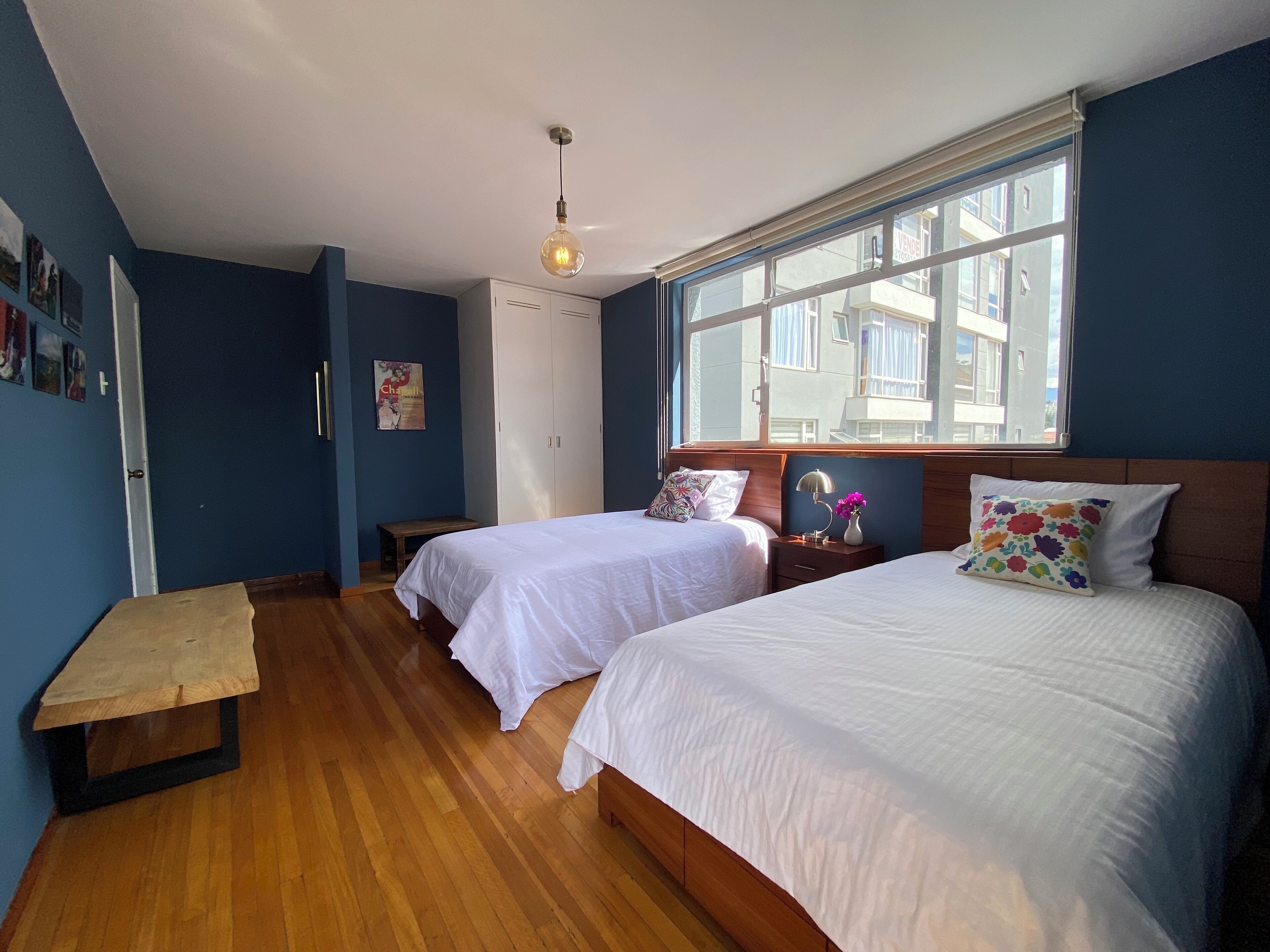 Un dormitorio con dos camas, un banco de madera, un escritorio y un ventanal grande.