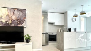 Une cuisine moderne avec des meubles blancs, un four encastré et un coin repas comprenant une table et des chaises blanches.