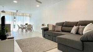Un salon moderne avec un canapé gris, une table basse blanche et un coin repas comprenant une table et des chaises blanches.