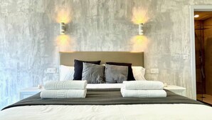 Une chambre d’hôtel avec un grand lit, deux lampes fixées au mur, une table de chevet et une porte de salle de bain.