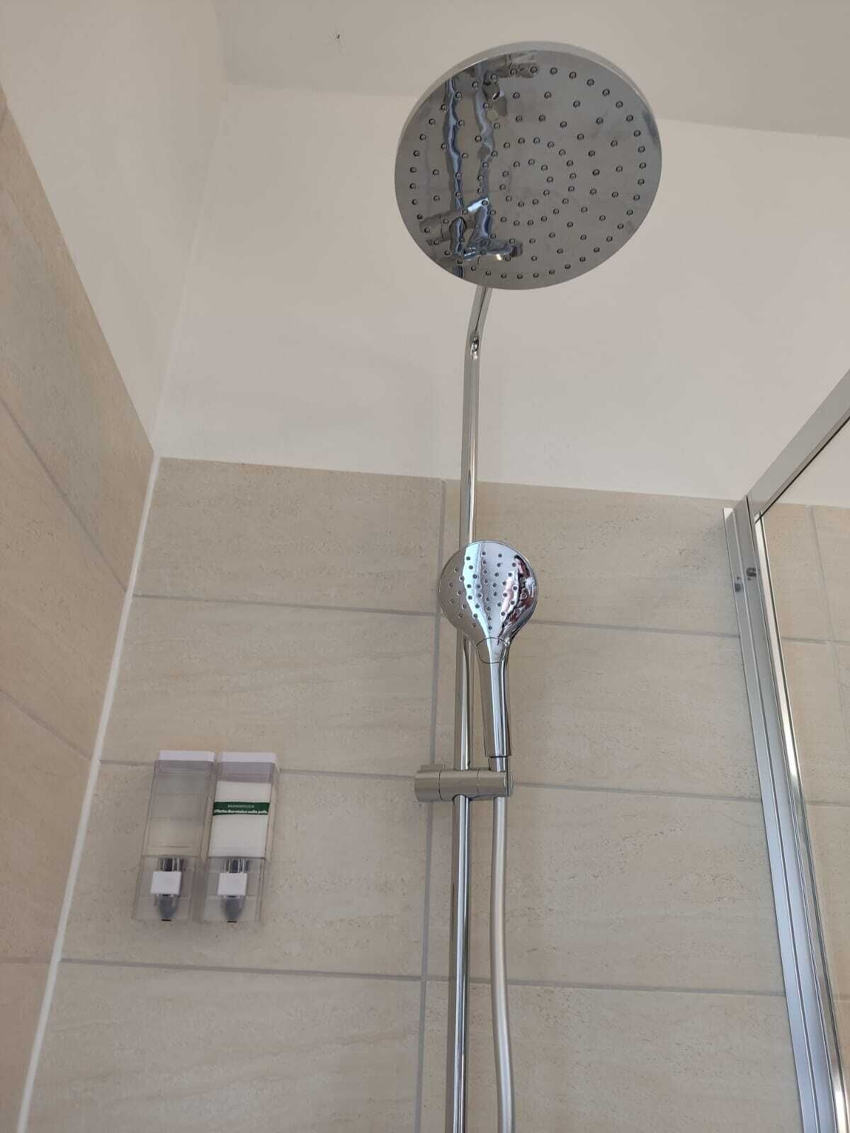 A shower with a round head, a handheld showerhead, and two soap dispensers on the wall.