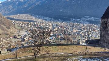 A town with a prominent stone tower, a river, and surrounding mountains.