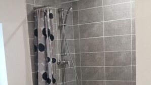 Douchegedeelte met een grijze betegelde muur, een douchekop en een gordijn met stippen.