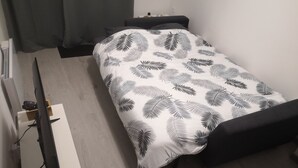 Een kleine, verzorgde slaapkamer met een bed, een bureau en een televisie.