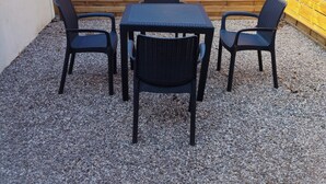 Een terras met een tafel en vier stoelen, omgeven door een houten hek en een grindpad.