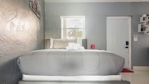A bedroom with a large bed, a window, a door, and a small shelf with items. - Cozy Studio in Miami (Miami)