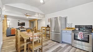 Una cocina moderna con un refrigerador de acero inoxidable, horno y una zona de comedor con mesa y sillas de madera.